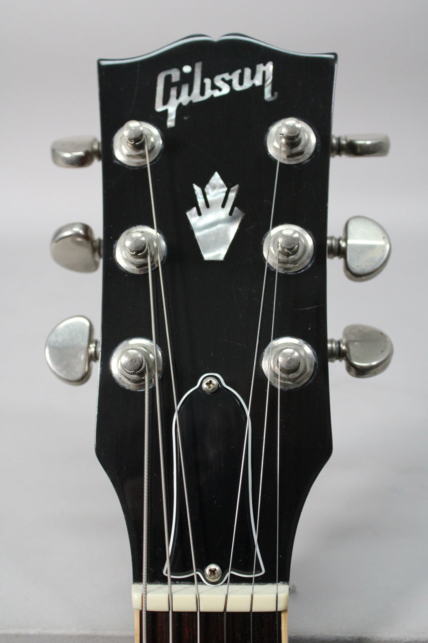Close-up of the black headstock with mother-of-pearl inlay, six chrome tuners, and a bell-shaped truss rod cover.