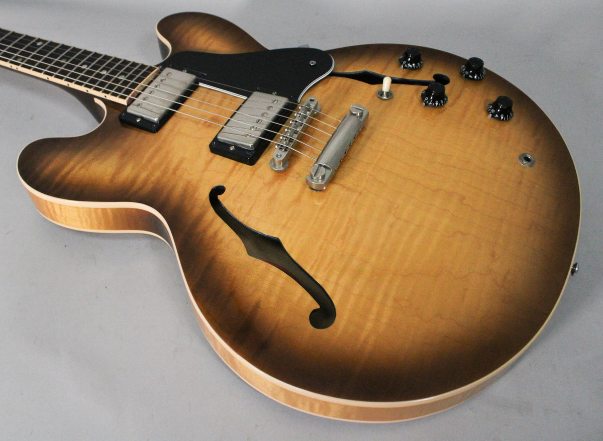 Upper body of a figured sunburst semi-hollow guitar, showing two humbuckers, a black pickguard, f-hole, and four black control knobs.