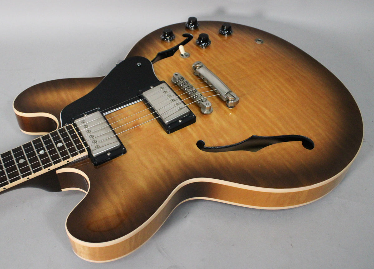 The sunburst semi-hollow guitar's body, with f-holes and a black pickguard, shows a figured maple top and nickel hardware.