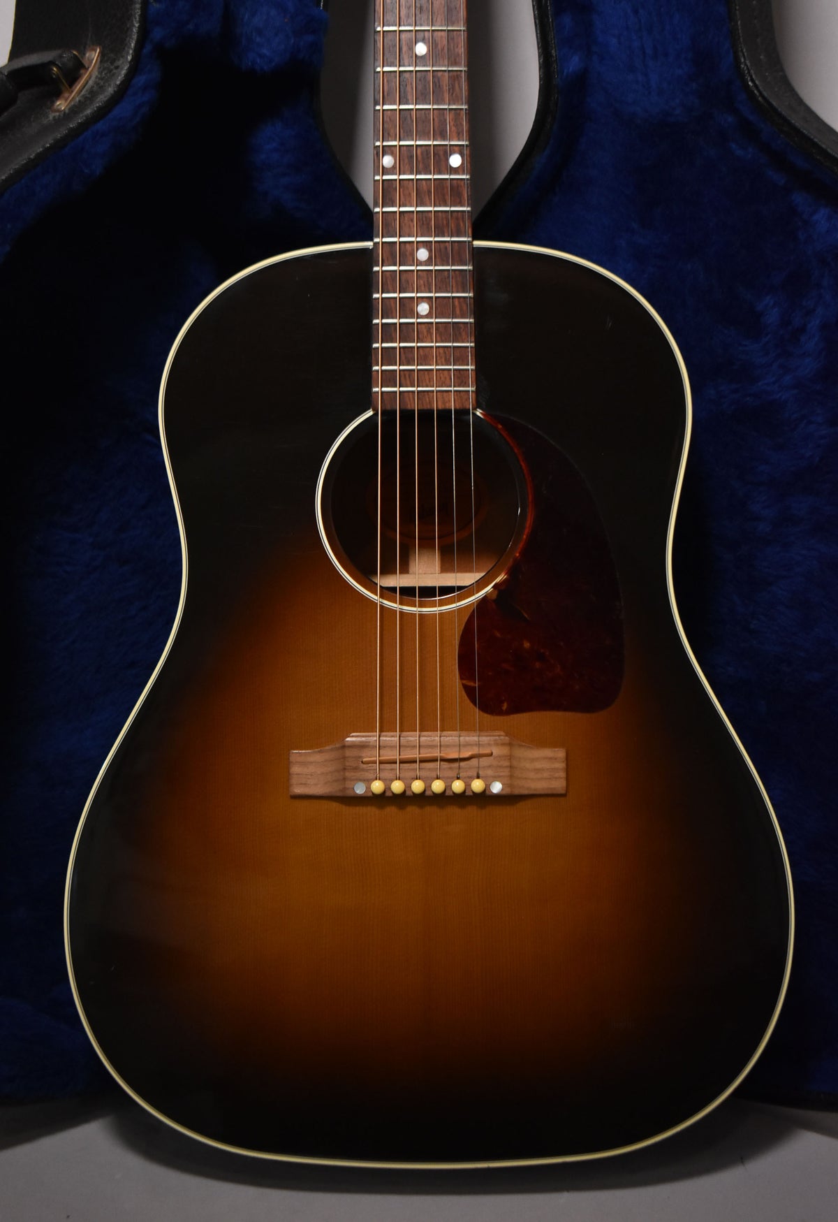 Full front view of a sunburst acoustic guitar, showing the body, pickguard, bridge, and lower fretboard.