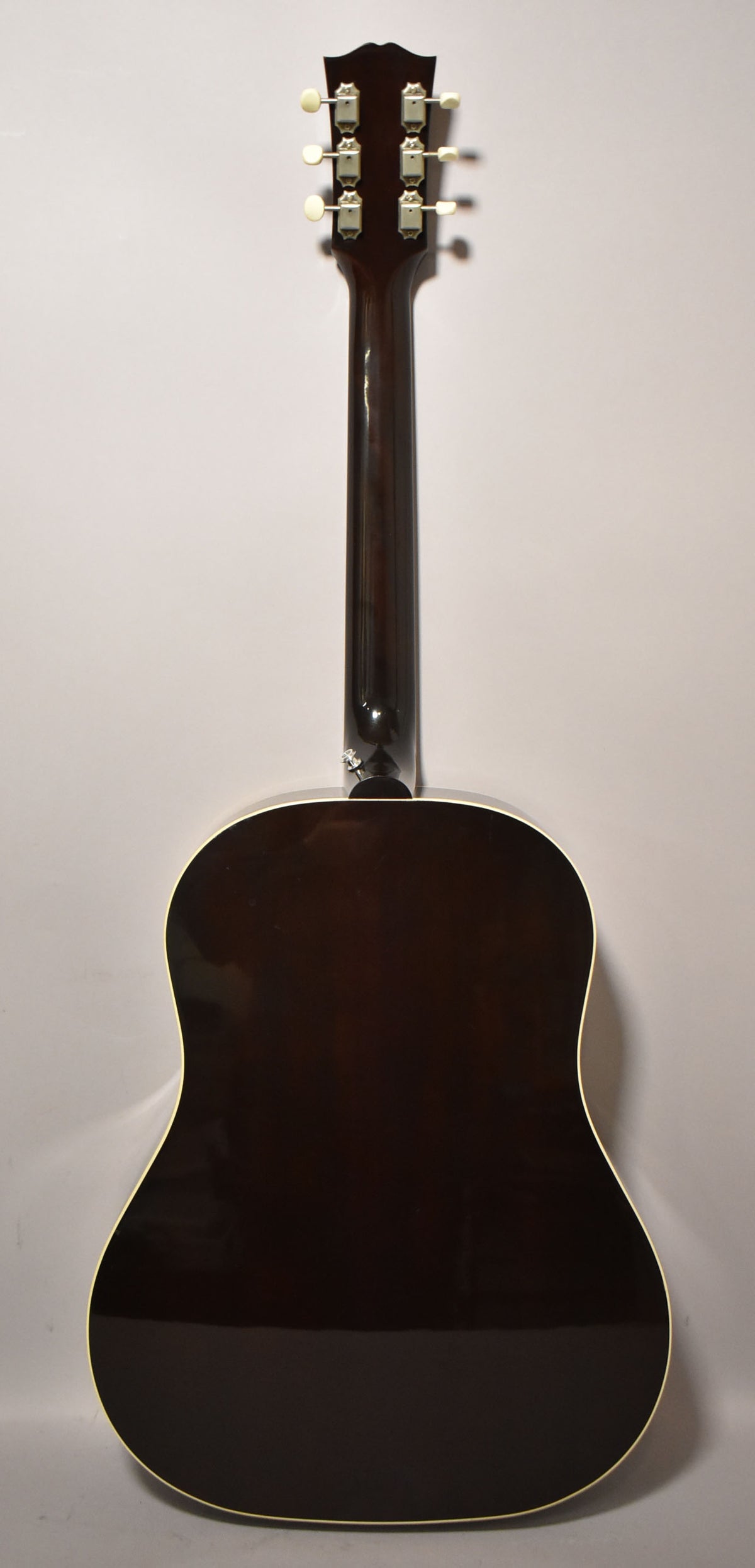 The guitar's dark sunburst back and neck are shown, with six cream tuning pegs on the headstock and a strap button at the heel.