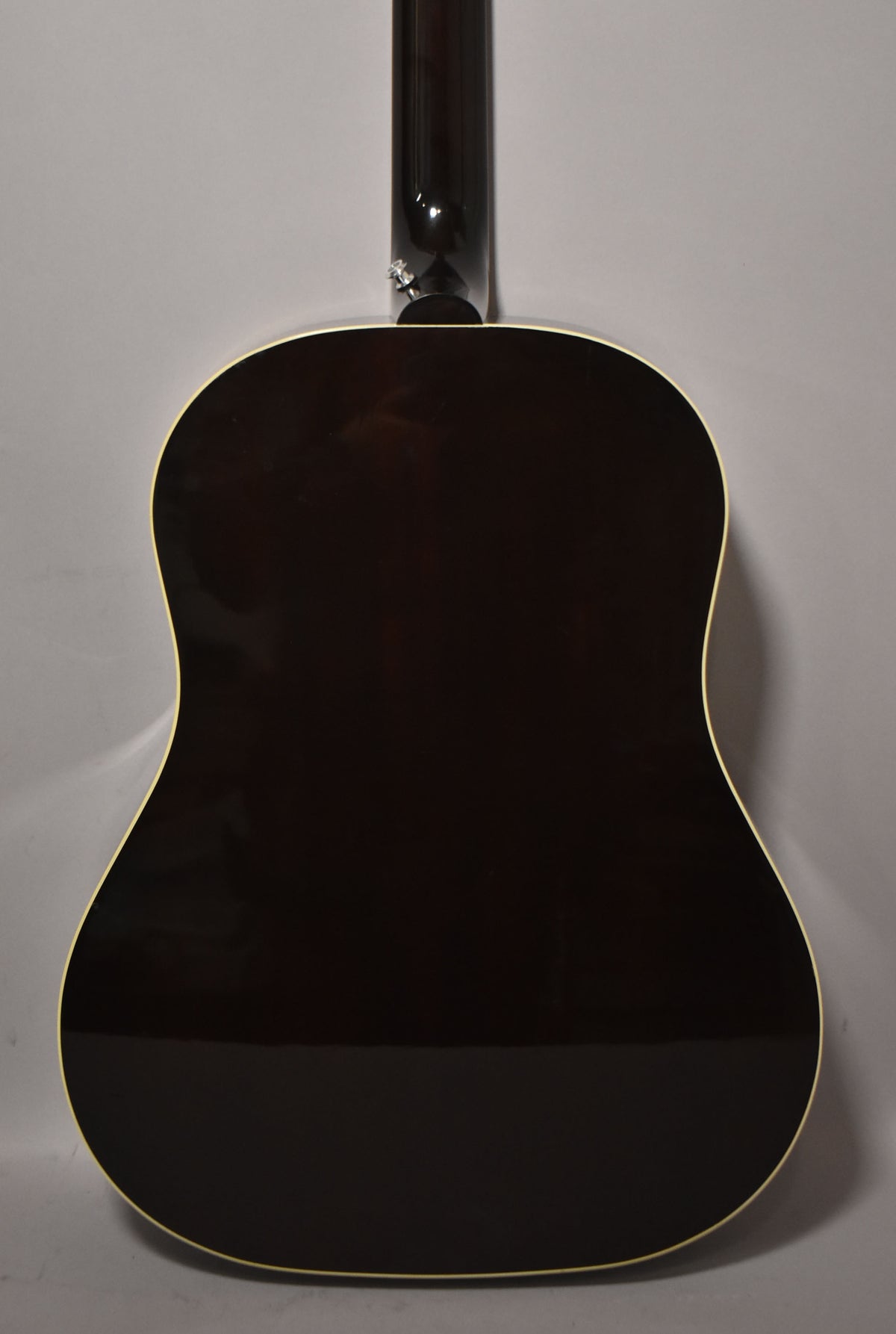The full back of the dark sunburst acoustic guitar is shown, with a strap button visible at the heel of the neck.