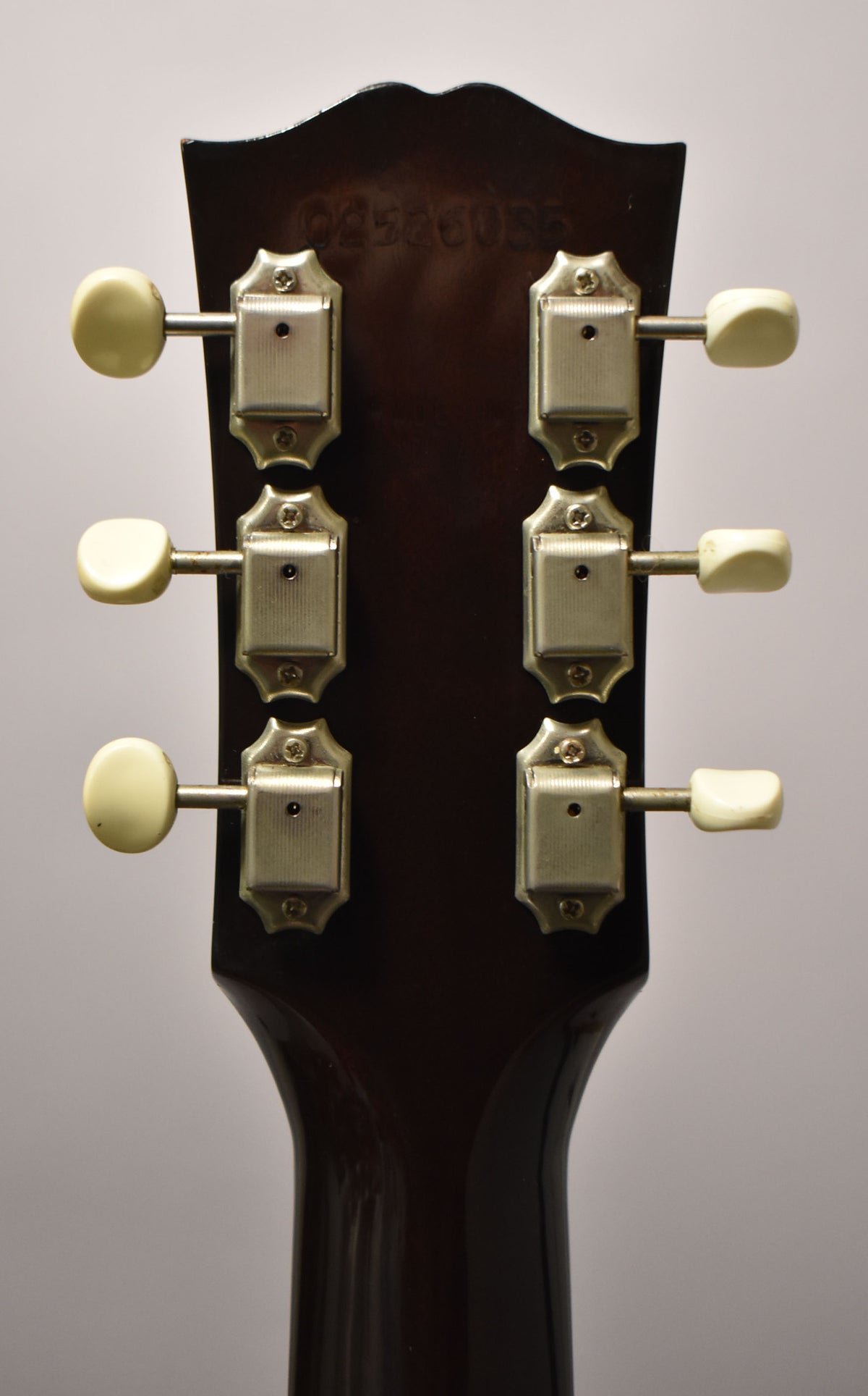 Rear view of the dark brown headstock and neck, showing six cream-colored tuning pegs and light wear on the neck.