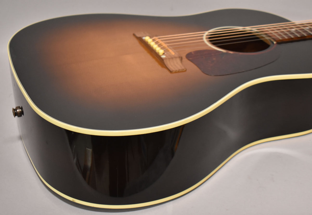 The acoustic guitar's lower bout and waist are framed, showing the sunburst top, dark sides, cream binding, and strap button.