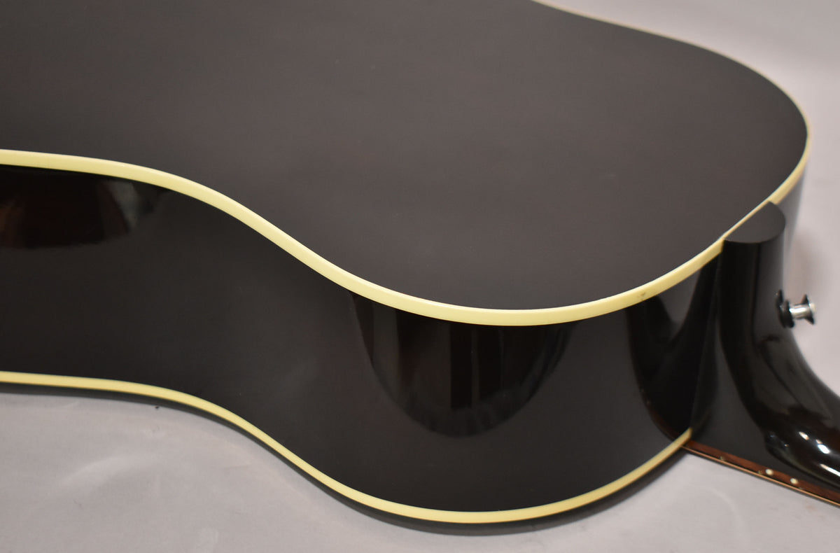 Upper bout and waist of a dark sunburst acoustic guitar, showing cream binding and a strap button on the heel.