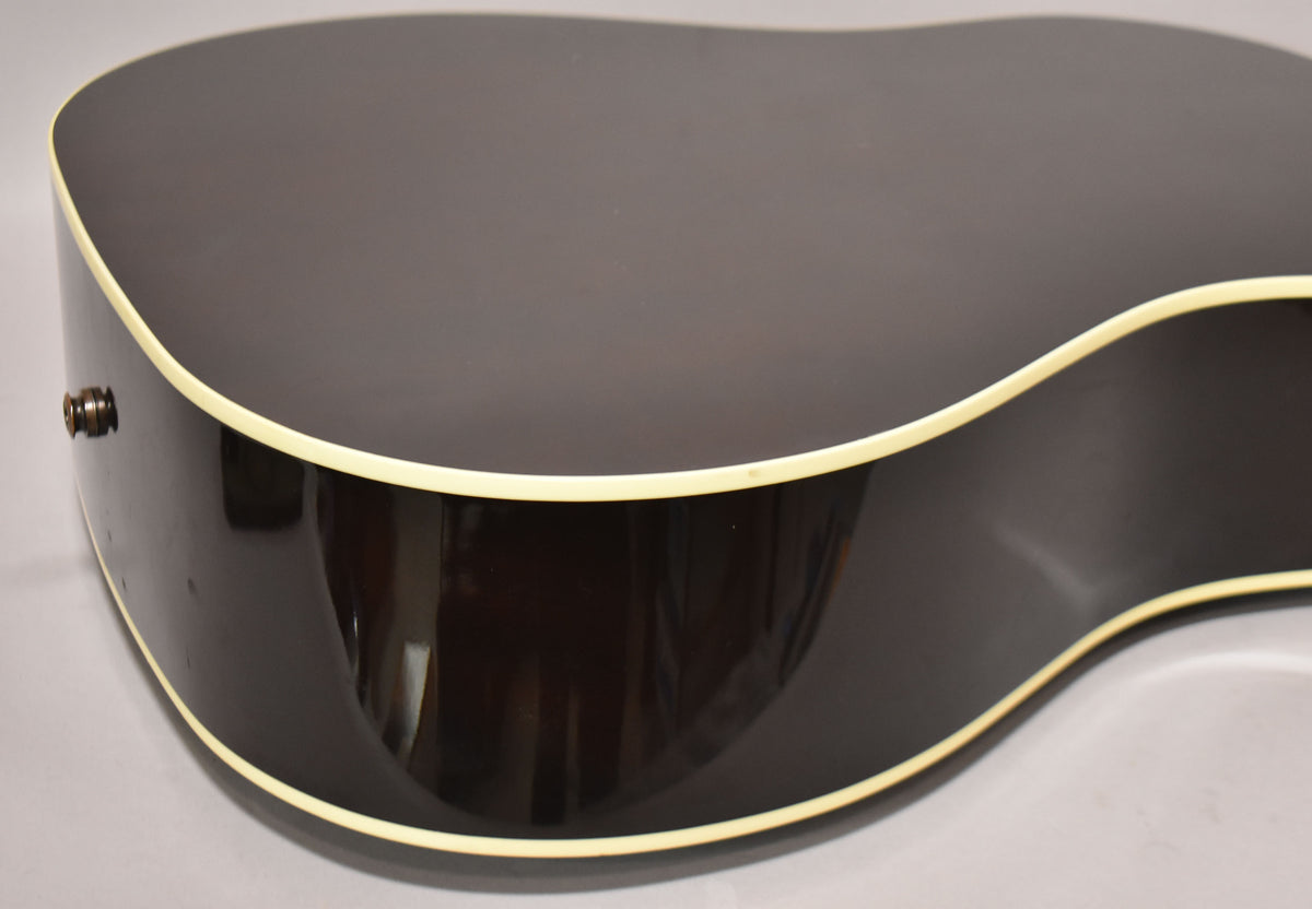 The lower bout of a dark sunburst acoustic guitar, showing the glossy finish, cream binding, and endpin jack.