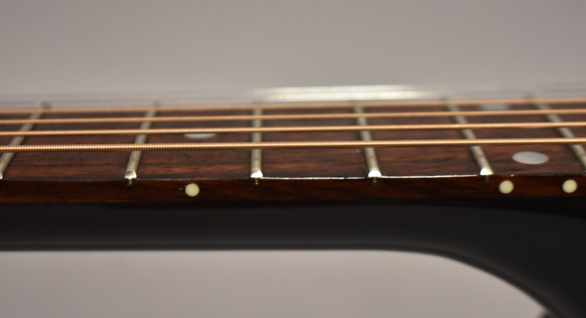 Close-up of the dark rosewood fretboard and frets, showing light wear and side dot markers, with bronze strings.