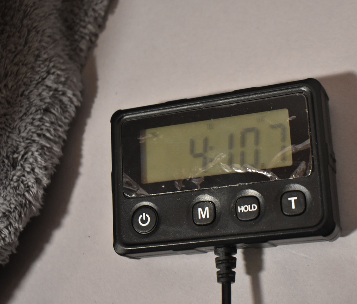 A black digital meter displays "4.10" on its screen, next to a gray fuzzy object.