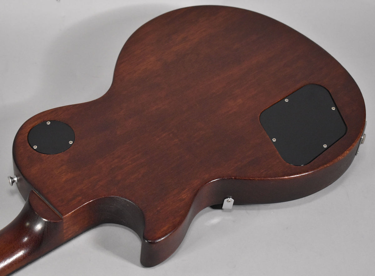 The back of a faded walnut Les Paul, showing the control cavity cover and switch access plate, with minor scuffs.