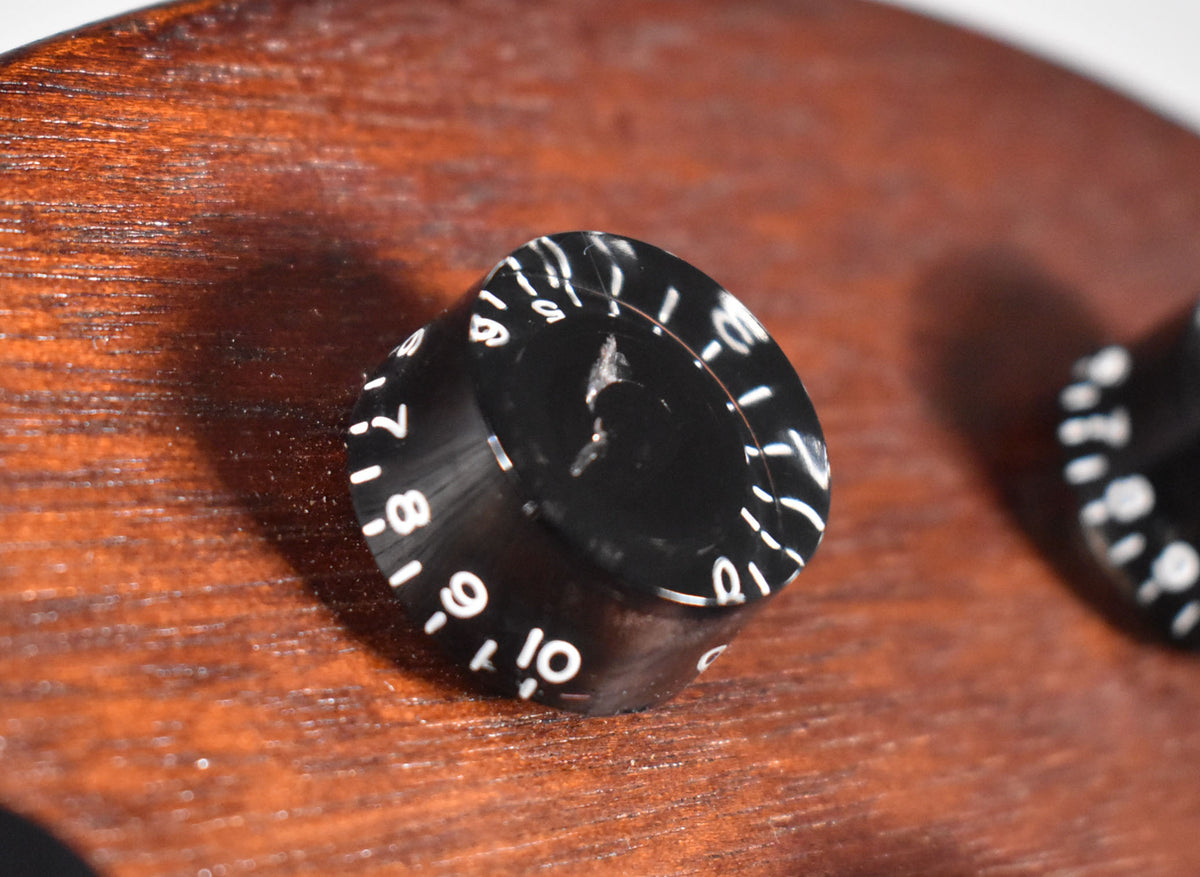 Close-up of a black top hat control knob with white numbers 0-10, showing a chip in the top, on a faded walnut body.