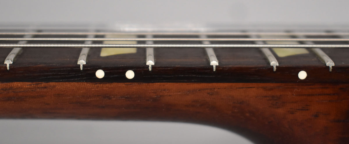 Close-up of the dark brown fretboard and neck, showing three white side dots and trapezoid inlays on the fretboard.