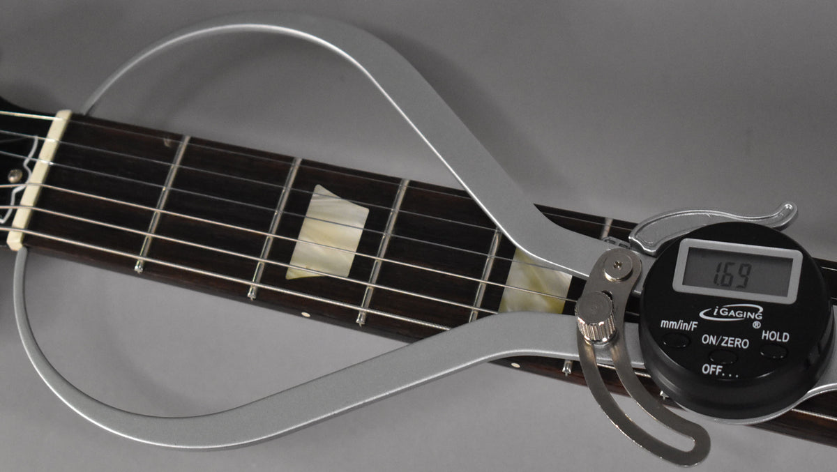 Close-up of the dark rosewood fretboard with trapezoid inlays, showing a digital string action gauge reading 1.69mm.