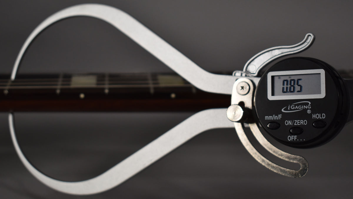 A digital caliper measures the dark brown fretboard, showing a reading of 0.85, with rectangular fret markers visible.