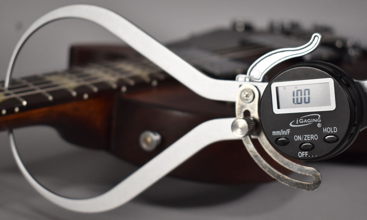 A digital caliper measures the nut width of the faded walnut guitar, showing "1.00" on its screen.