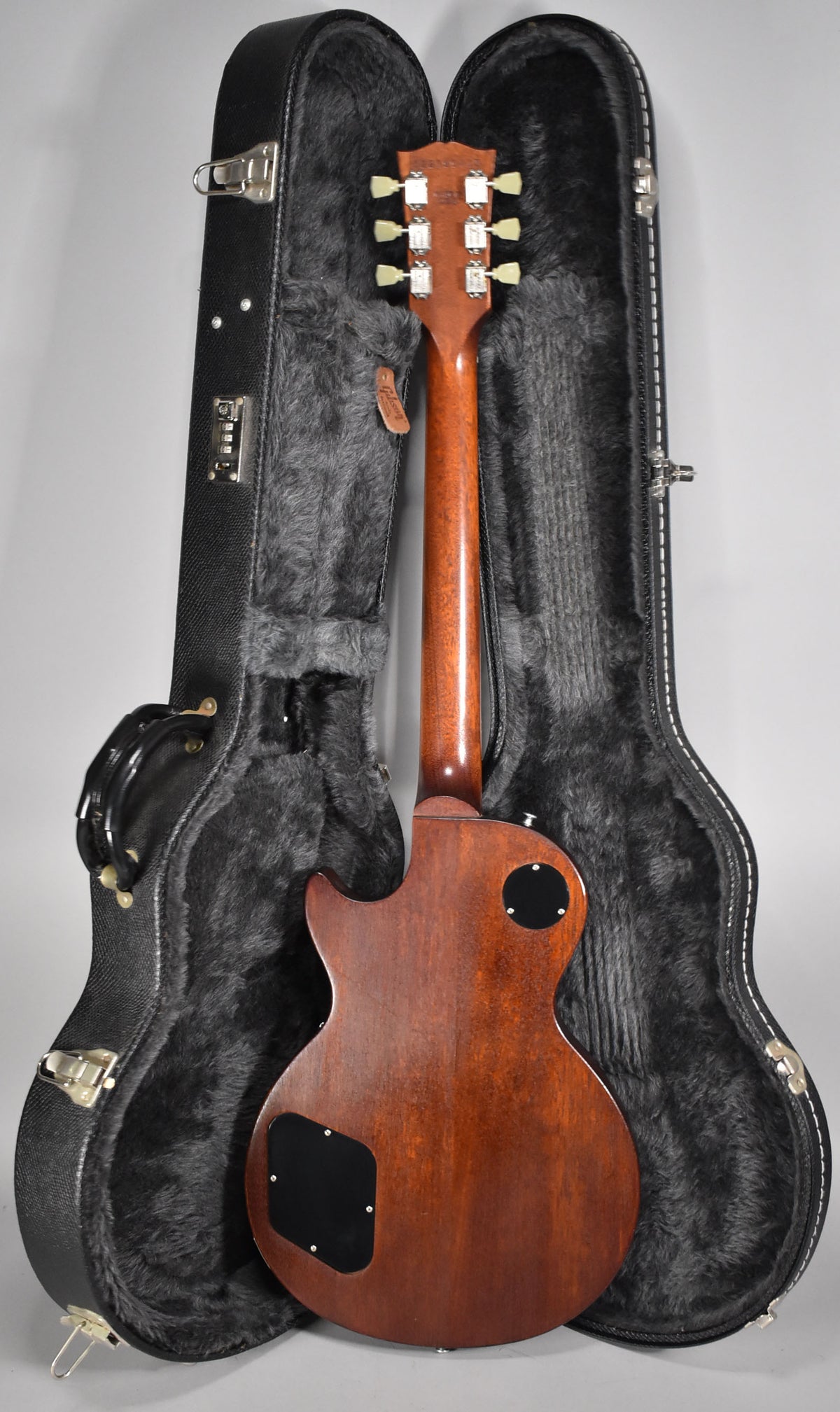 The guitar's faded walnut back and neck are visible, with six cream tuners on the headstock, resting in its open, black fur-lined hard case.