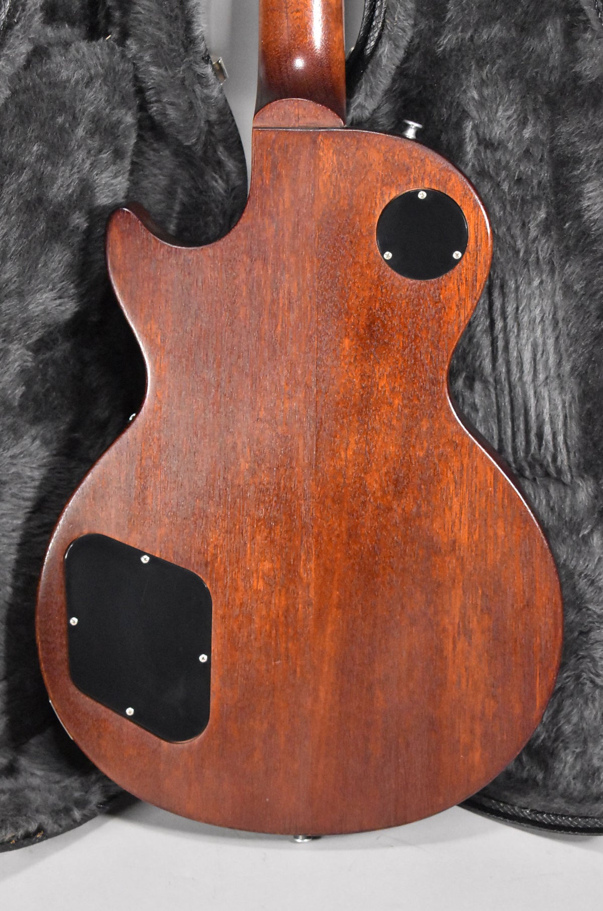 The guitar's back, a faded walnut with visible wood grain, shows two black control cavity covers and a strap button.