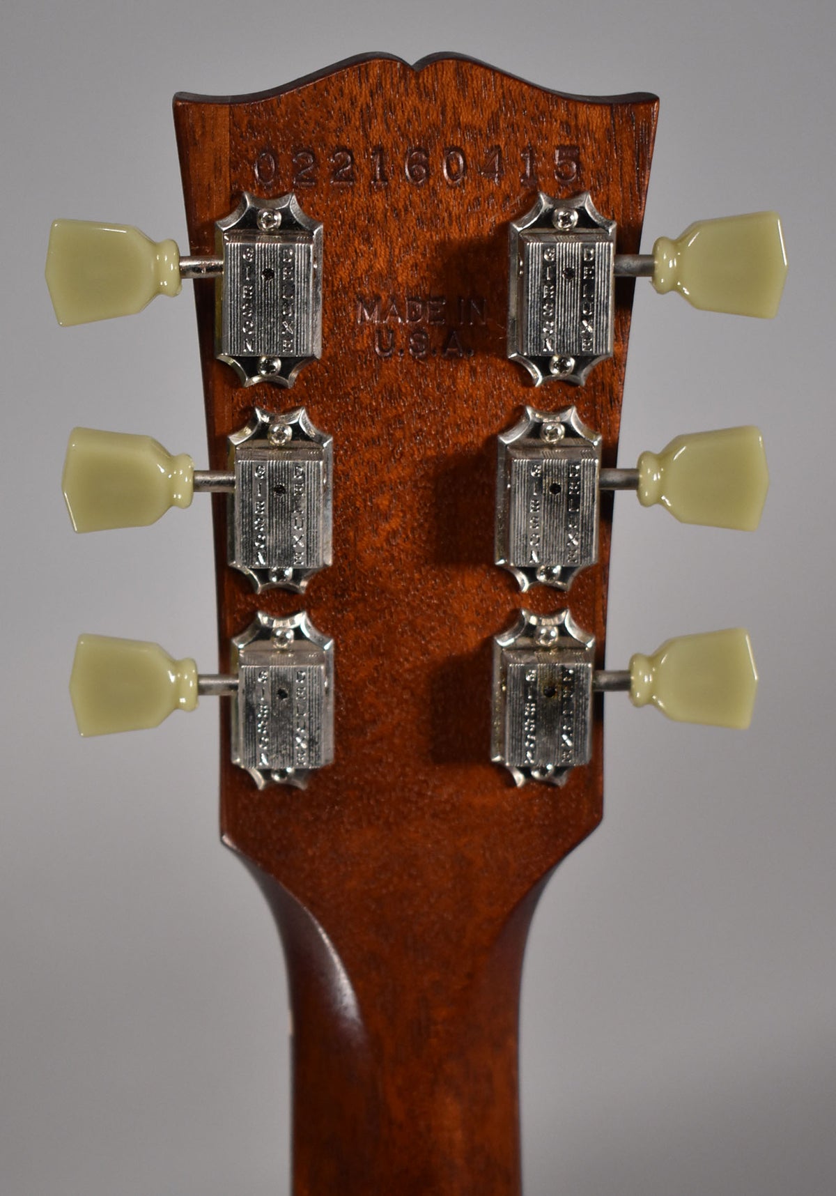The back of a faded walnut headstock with six cream-buttoned, nickel-plated tuners, showing light wear and a serial number.