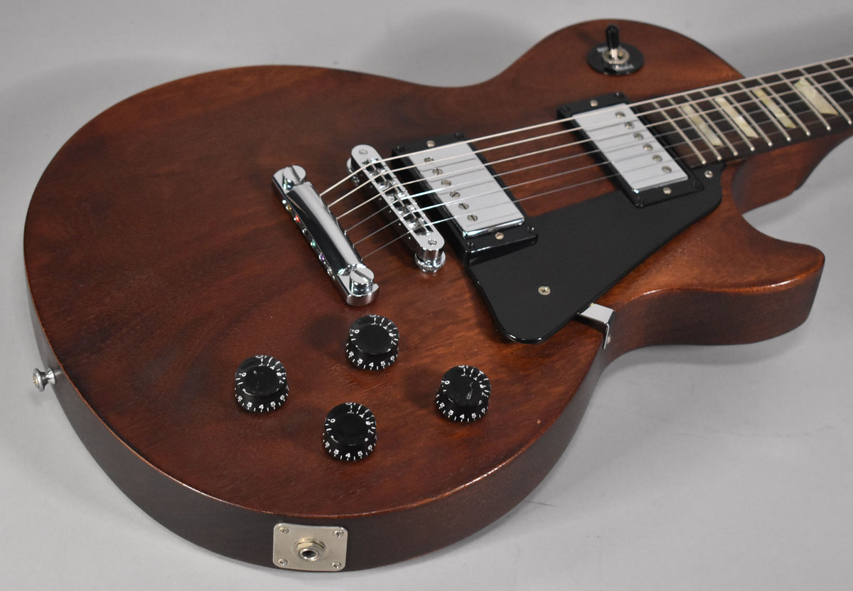 The faded walnut guitar body, with a black pickguard and chrome hardware, is angled to show the four black control knobs.