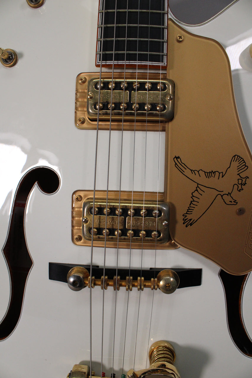 Close-up of the white guitar body, showing gold humbuckers, a gold pickguard with a falcon graphic, and an f-hole.