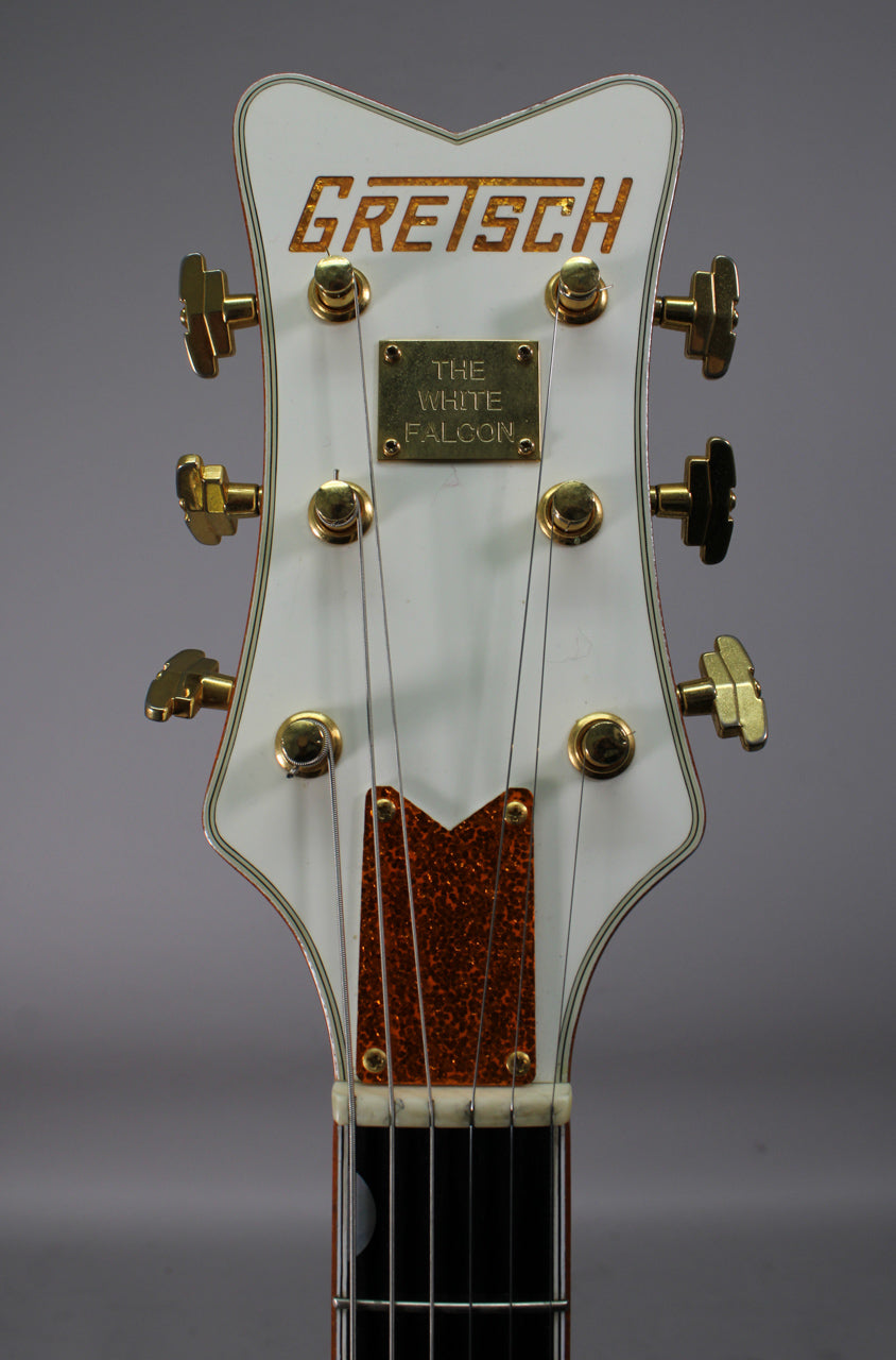 The white headstock, with gold tuners and a gold "The White Falcon" plaque, shows light wear and a glittery orange truss rod cover.