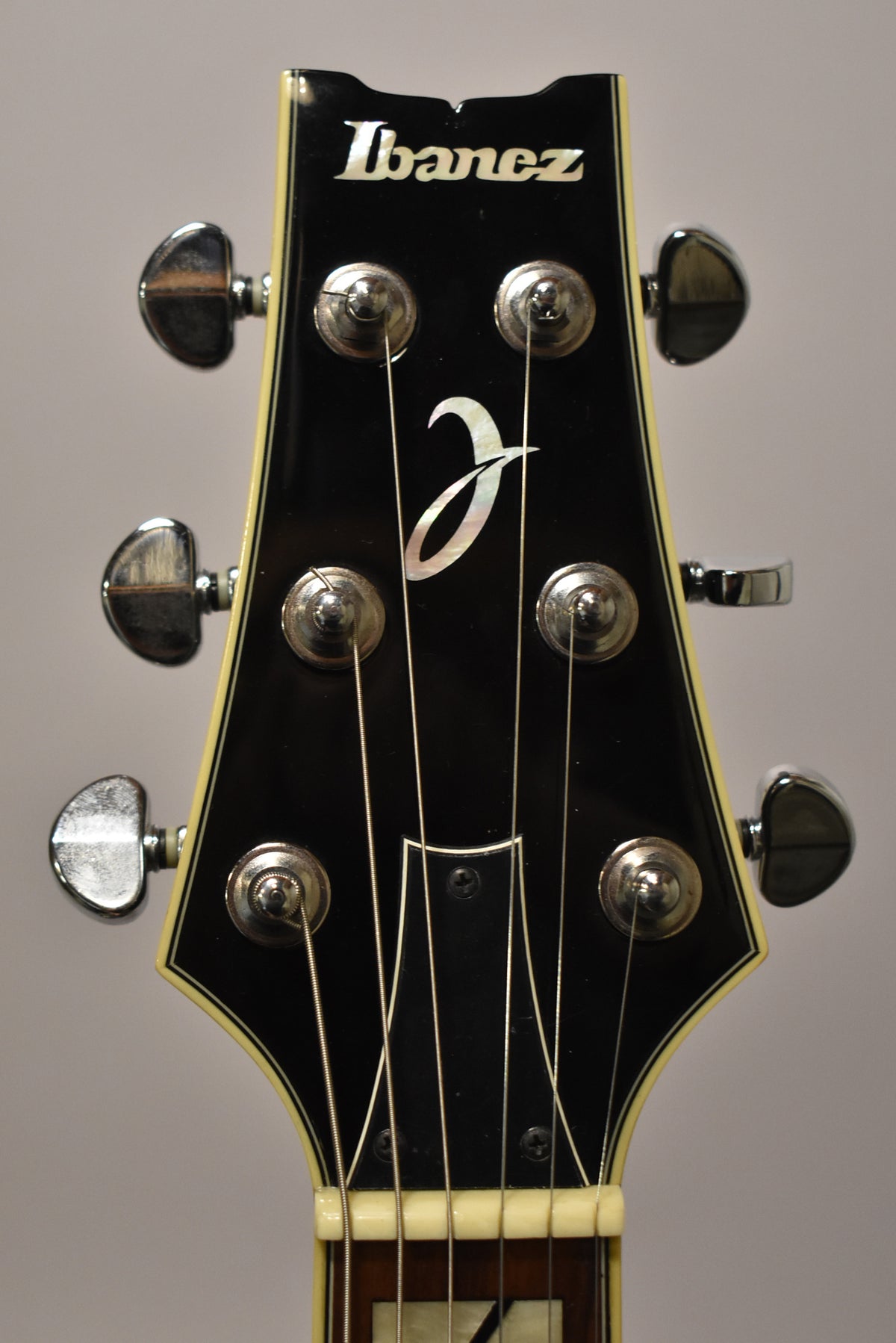 Close-up of the guitar's black headstock with cream binding, showing six chrome tuners, a pearloid logo, and the top of the nut.