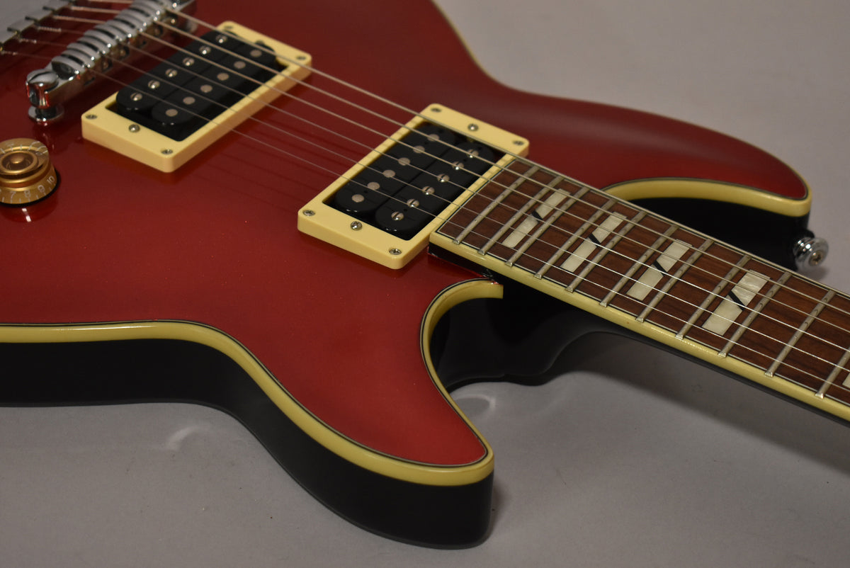 Close-up of the candy apple red body, showing cream-bound black sides, two humbuckers with cream surrounds, and a dark fretboard.
