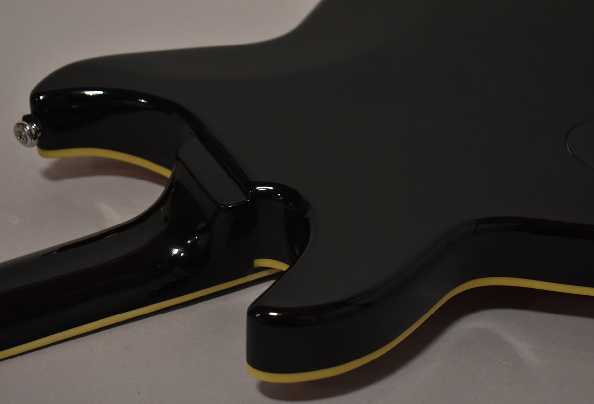 Close-up of the guitar's glossy black body and neck joint, with cream binding visible along the edges and a chrome strap button.