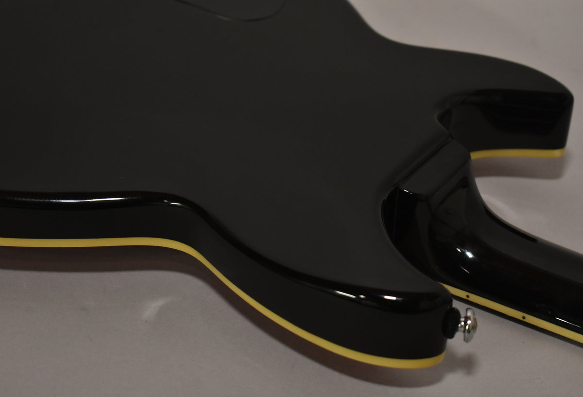 The guitar's black body with cream binding and a chrome strap button is seen from the lower bout, angled towards the neck joint.