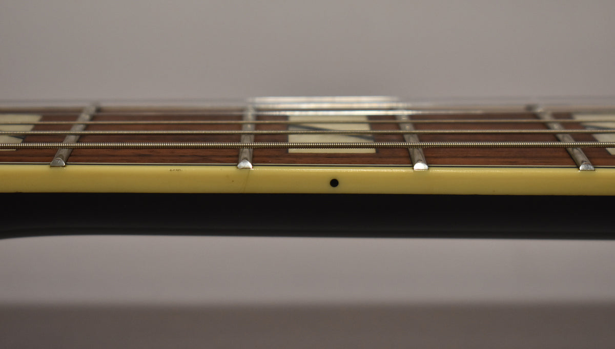 Close-up of the guitar's fretboard from the side, showing dark wood, metal frets, cream binding, and a small black dot inlay.