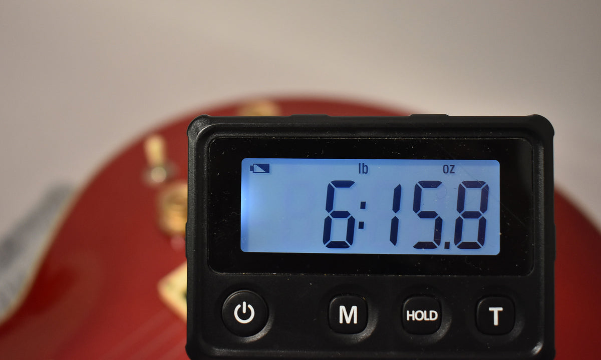 A digital scale displays "6:15.8 lb oz" with a red guitar body visible in the blurred background.