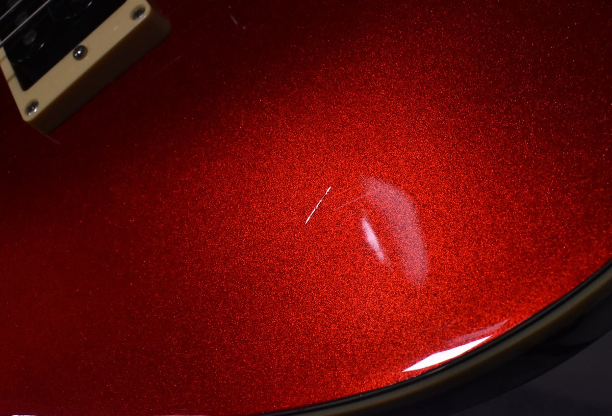 Close-up of the guitar's metallic candy apple red finish, showing a visible scratch and light reflections on the lower bout.