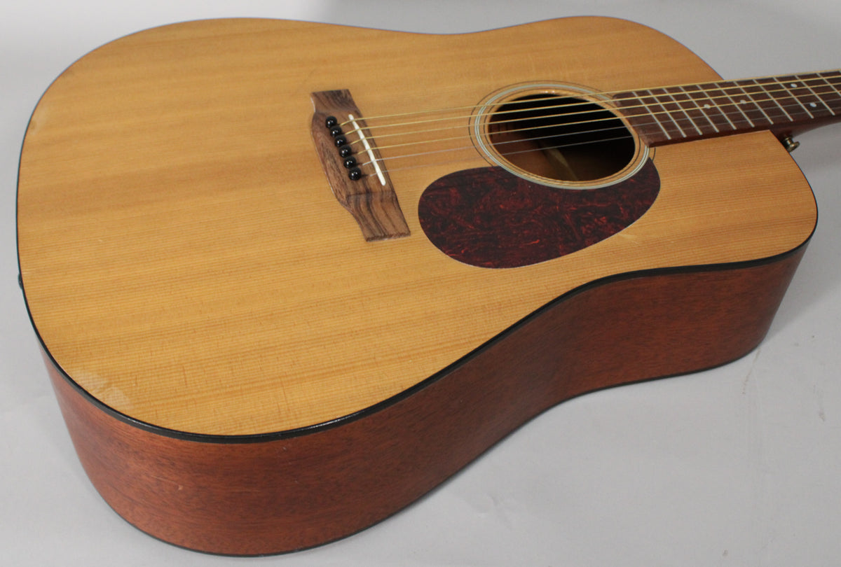 The acoustic guitar's light wood top and dark mahogany sides are visible from the upper bout, with a tortoiseshell pickguard and dark bridge.