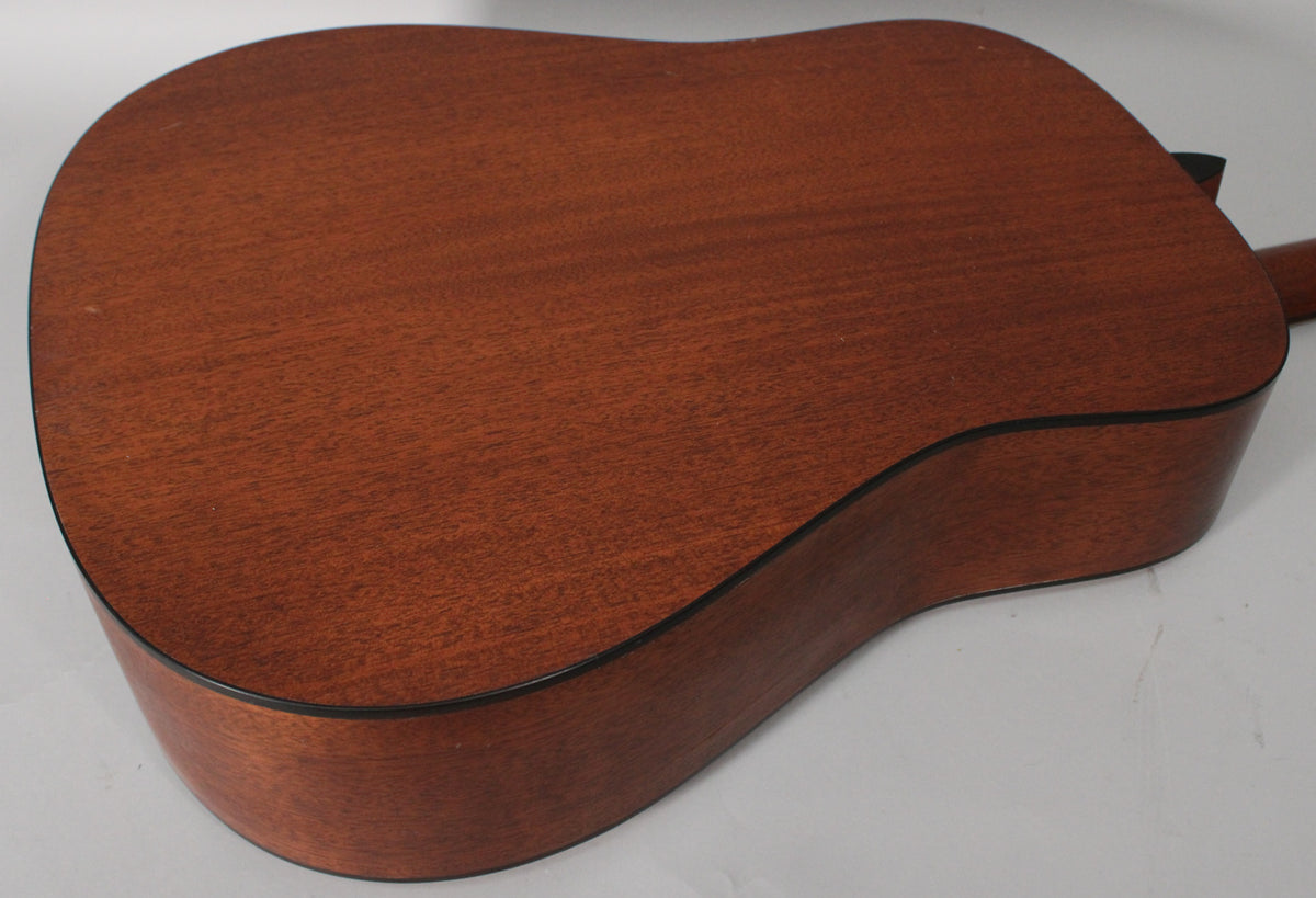 The back of a satin mahogany acoustic guitar, angled from the lower bout, showing light wear and wood grain.