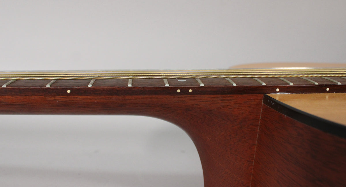 Close-up of the guitar's mahogany neck and dark fretboard, showing dot inlays and light strings, with some minor finish wear.