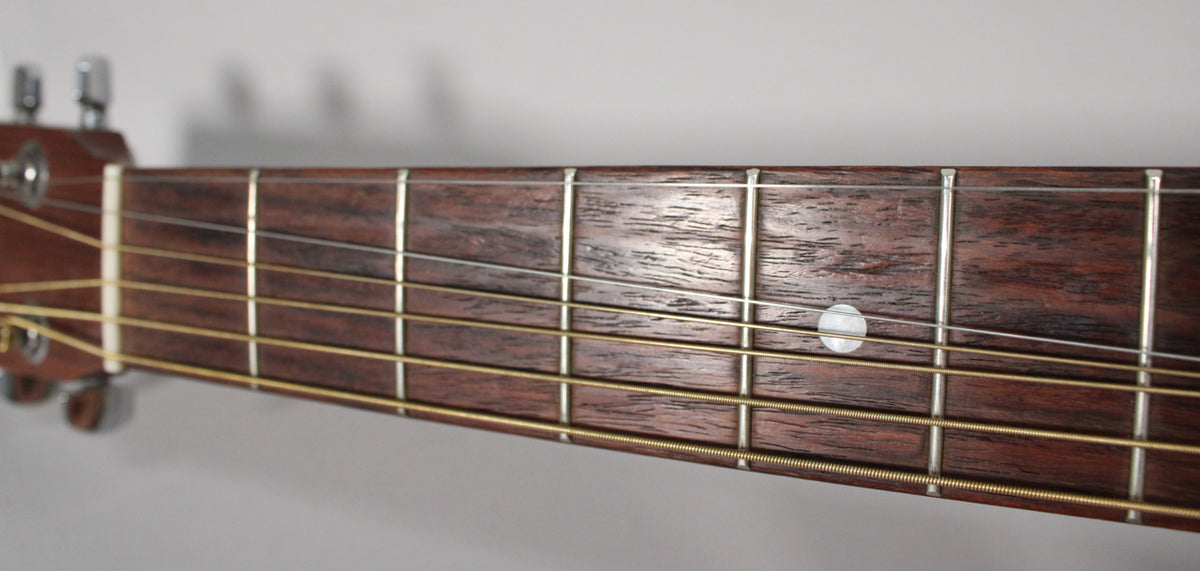 Close-up of the dark brown fretboard with a single pearl dot inlay at the 7th fret, showing light wear and gold strings.