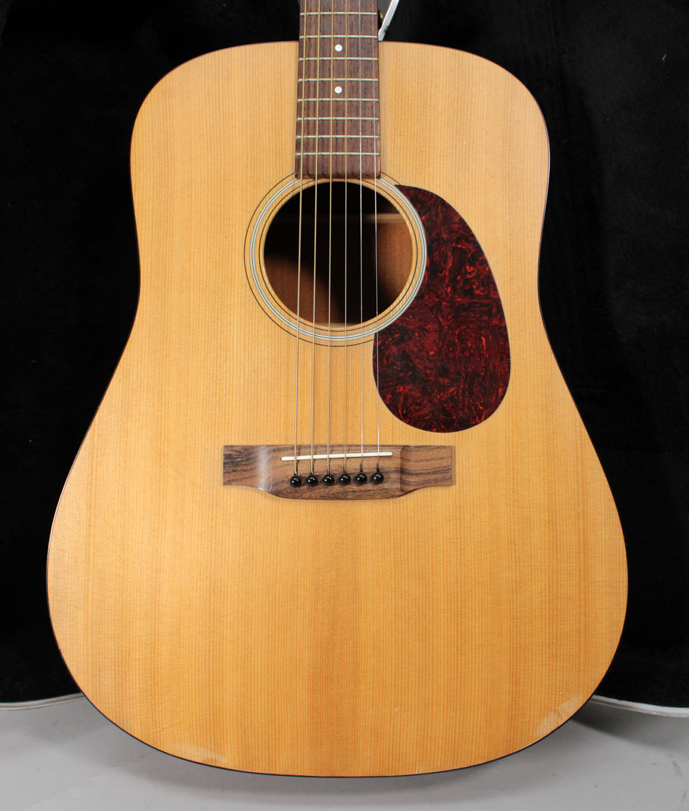 Full front view of a light-colored acoustic guitar with a dark tortoiseshell pickguard and a dark wood bridge.