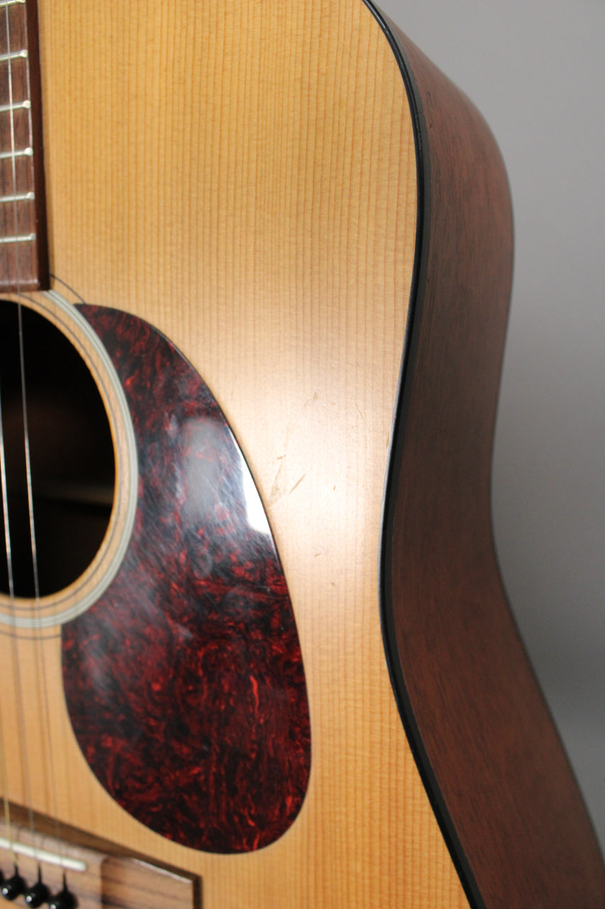Close-up of the acoustic guitar's light-colored satin top and dark mahogany side, showing a tortoiseshell pickguard and light scratches.