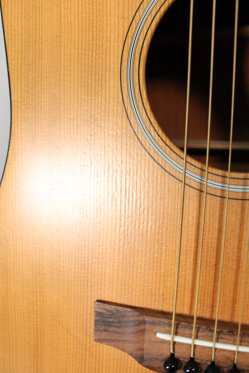 Close-up of the light wood body with vertical grain, showing the soundhole with concentric rings and a dark wood bridge with black pins.