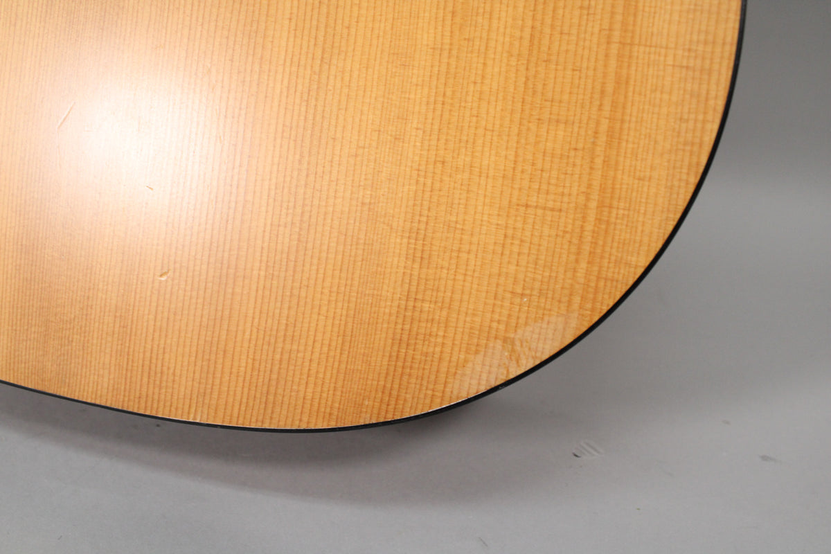 Close-up of the light brown, satin-finish acoustic guitar body, showing faint vertical grain and a few small dings.