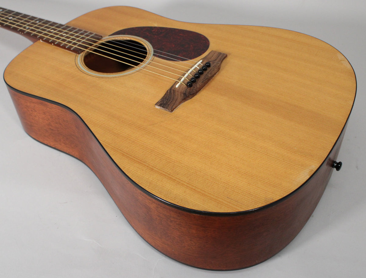 The dreadnought acoustic guitar is angled from the upper left, showing its light satin top, dark mahogany sides, and a black end pin.