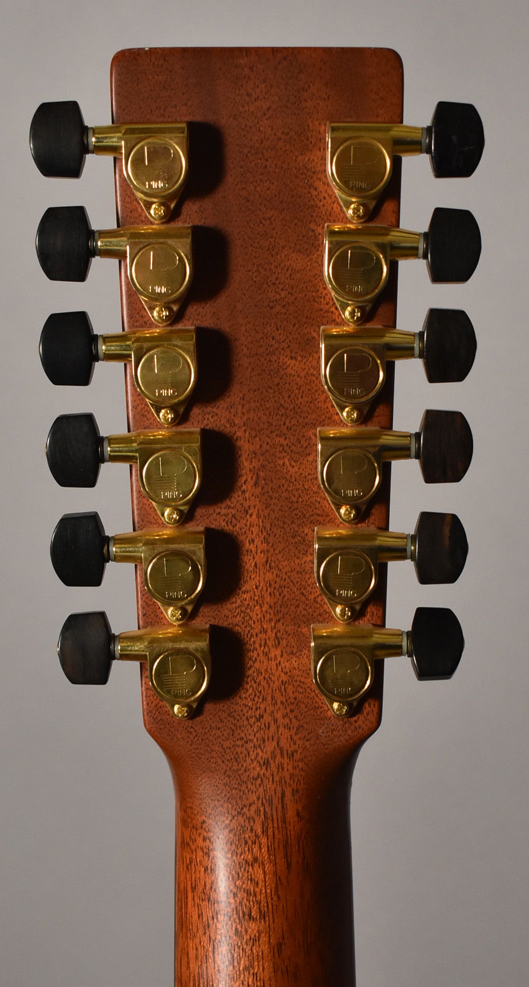 Rear view of the headstock and upper neck, showing twelve gold tuners with black buttons on a mahogany finish.