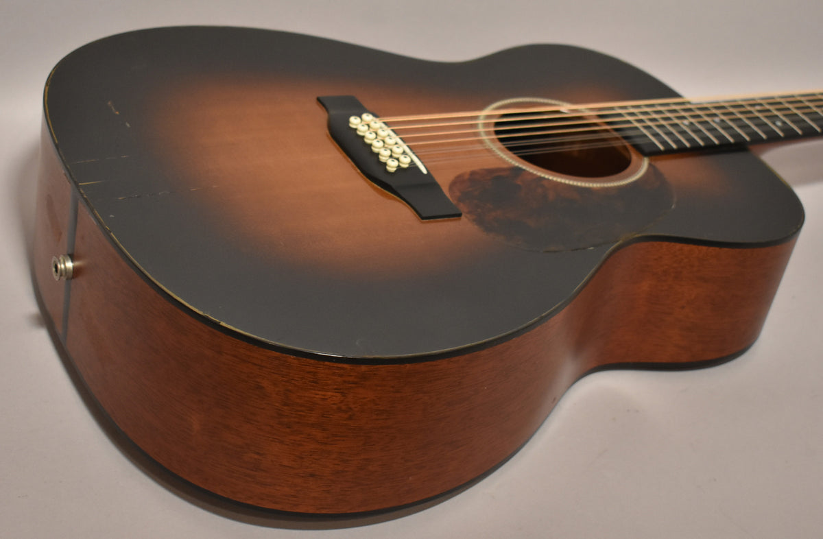 The 12-string guitar's sunburst top shows wear and checking along the lower bout, with a visible endpin jack.