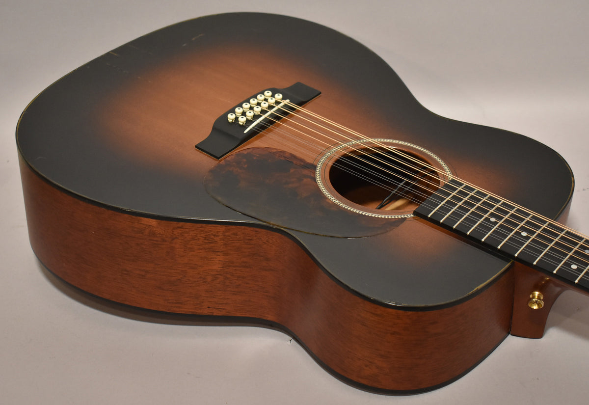 The 12-string jumbo guitar's sunburst top shows wear on the upper bout, with a tortoiseshell pickguard and white binding.