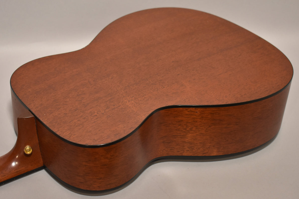 The guitar's back and side are visible, showing a reddish-brown wood grain with a satin finish and black binding.