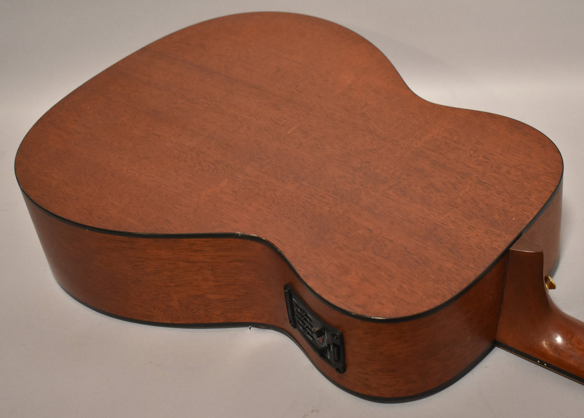 The guitar's mahogany back and sides are visible, with a black preamp control panel on the upper bout and a strap button near the neck heel.