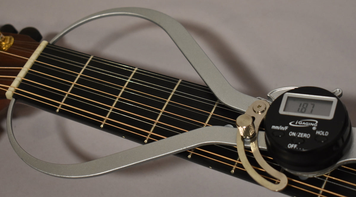 A digital caliper measures the nut width of the 12-string guitar's dark fretboard, displaying "1.87".