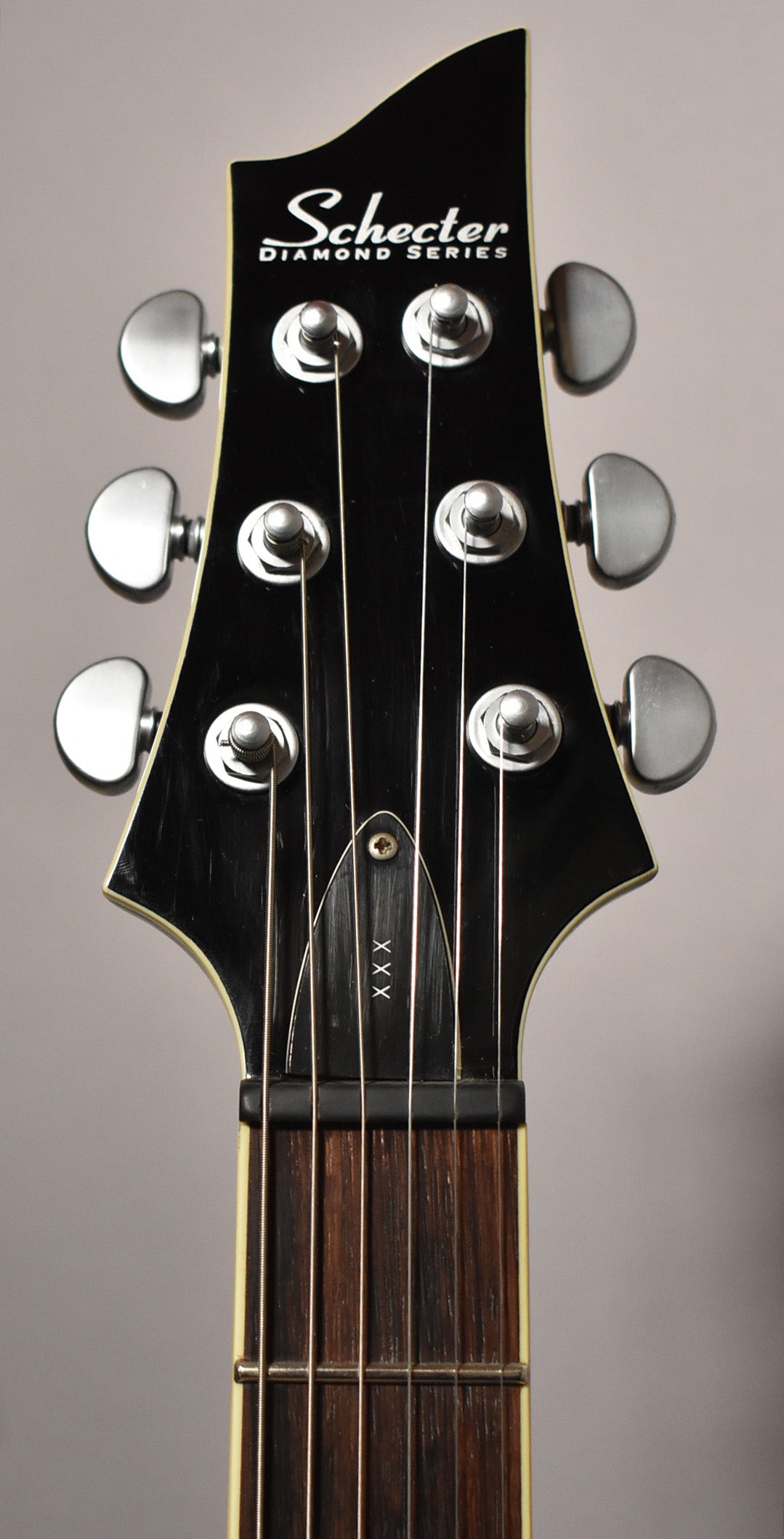 Close-up of the black gloss headstock with six chrome tuners, showing light scratches and a cream binding along the edge.