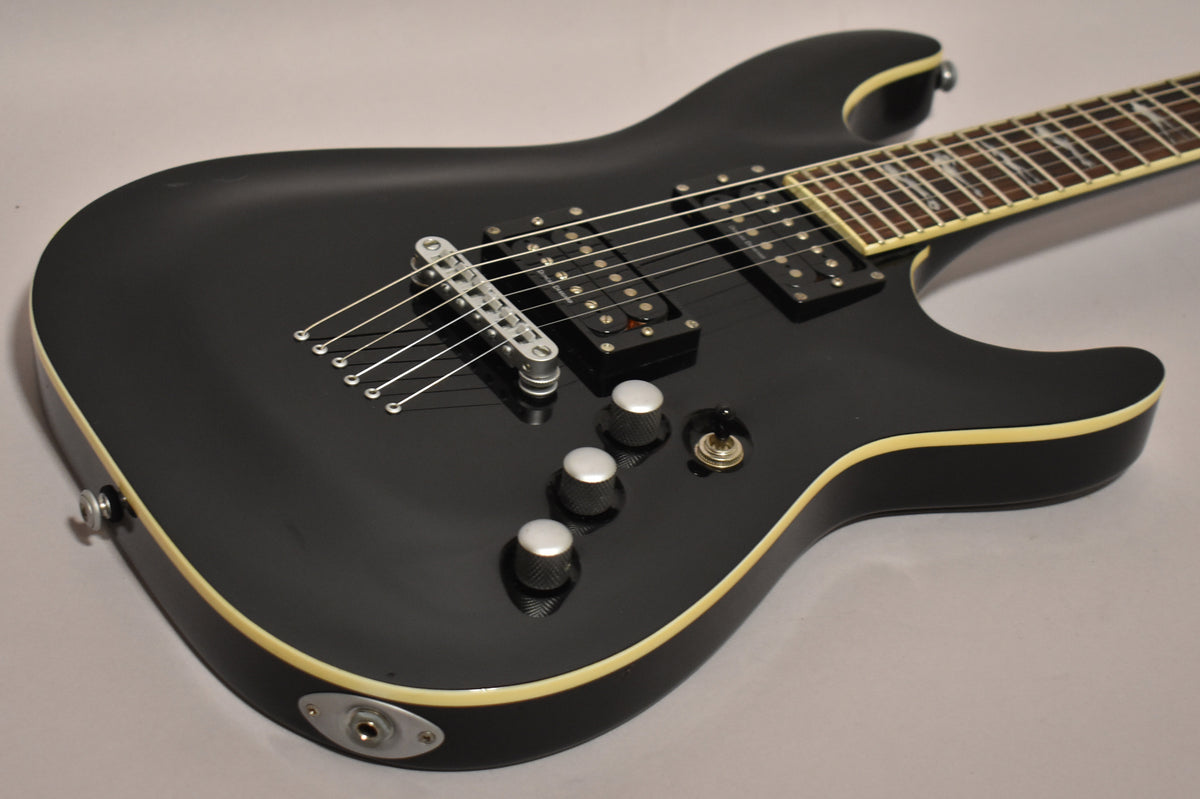 The black electric guitar, with cream binding, shows its body and lower neck, with three silver knobs and a toggle switch.