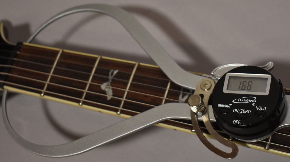 A digital caliper measures string height at 1.86mm on the dark fretboard with bird inlays and cream binding.