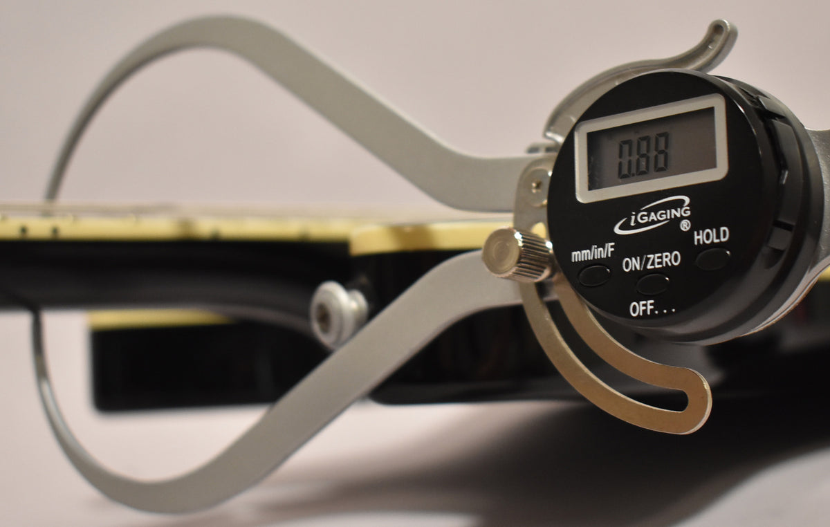 A digital caliper measures the black guitar's fretboard, showing a 0.88mm reading on its display.